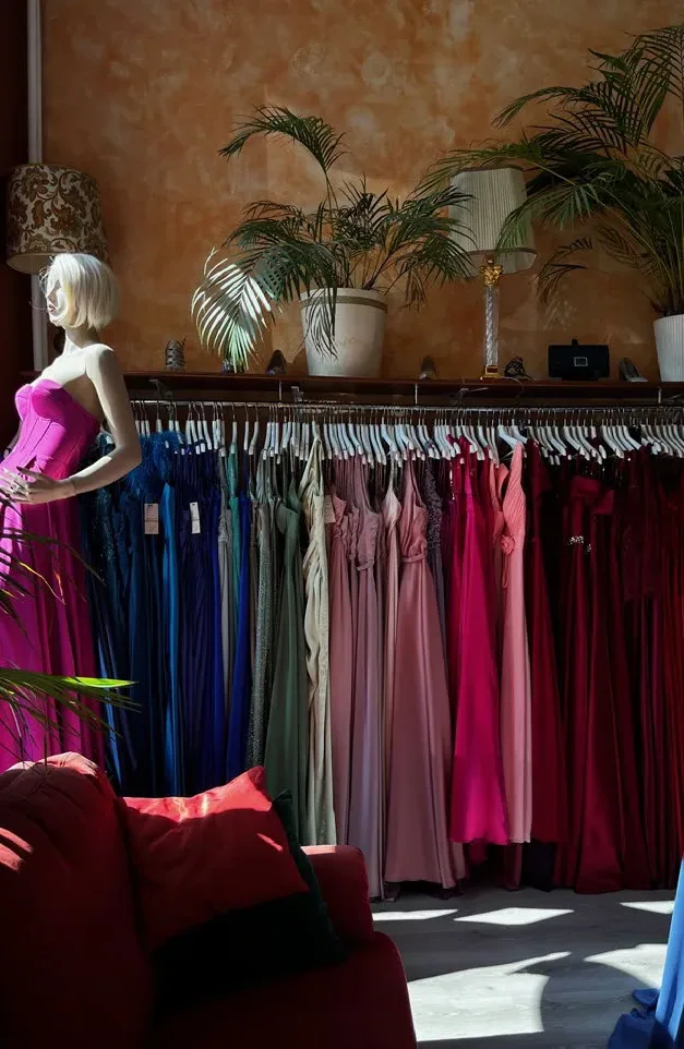 Rayon de LK Boutique : robes de soirée rangées par couleur, du bleu au rouge, près d'un mannequin en robe rose